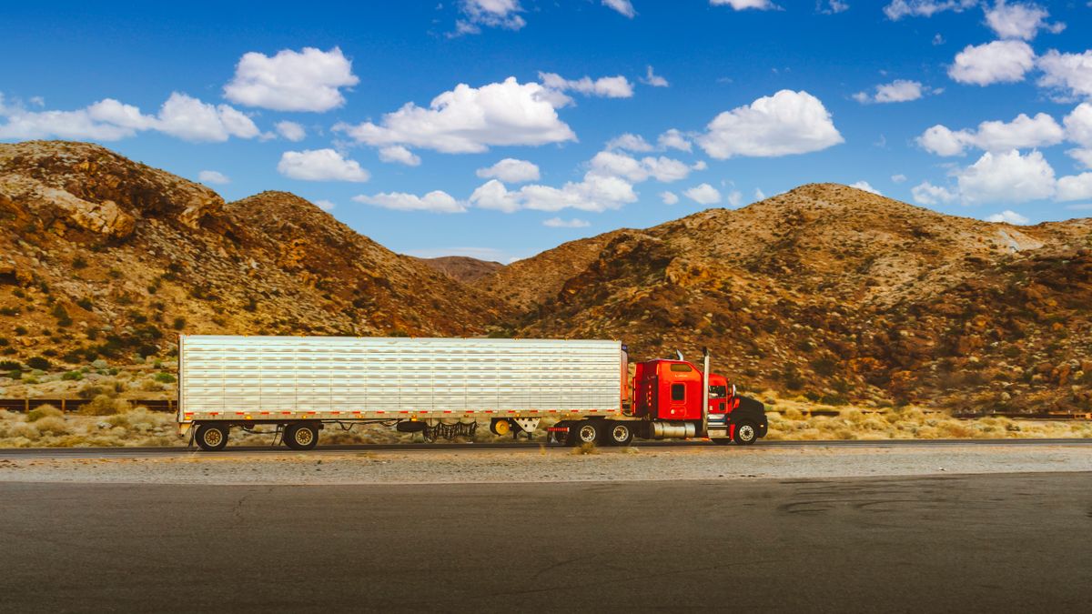 Red semi-truck traveling a desert highway with mountain views