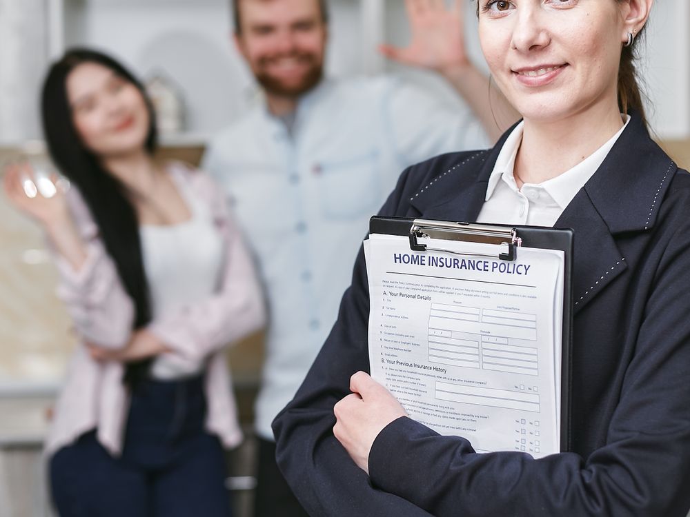 Friendly insurance agent holding a home insurance policy with a family behind