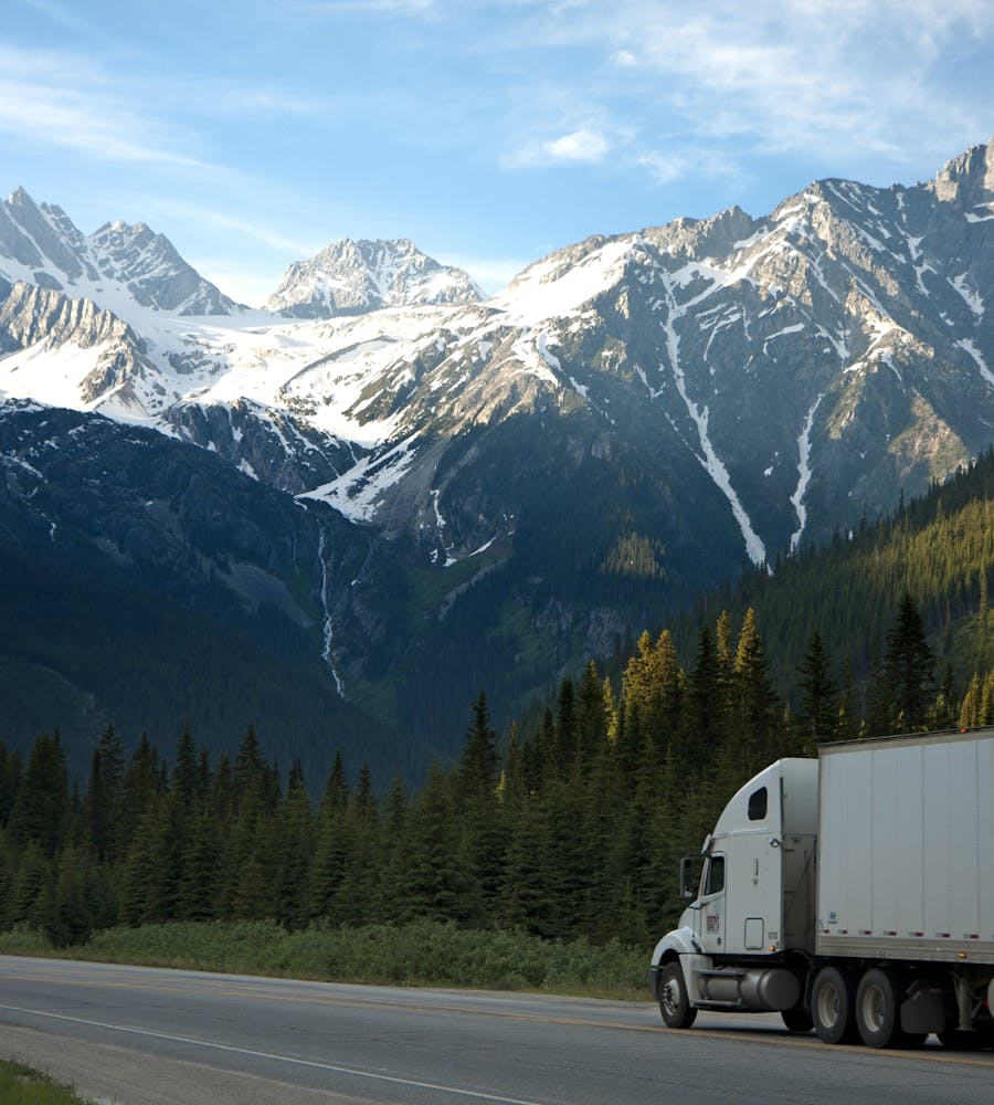 Semi truck on a highway through snow-capped mountains